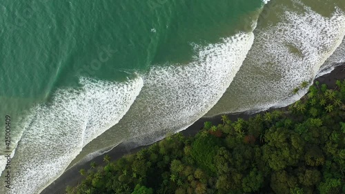 Aerial top shot Costa Rica Beautiful series of waves breaking on a black sand beach tropical jungle photo