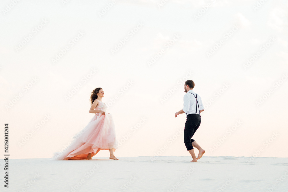 young couple a guy in black breeches and a girl in a pink dress are walking along the white sand young couple a guy in black breeches and a girl in a pink dress are walking along the white sand