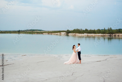 young couple a guy in black breeches and a girl in a pink dress are walking along the white sand © omelnickiy
