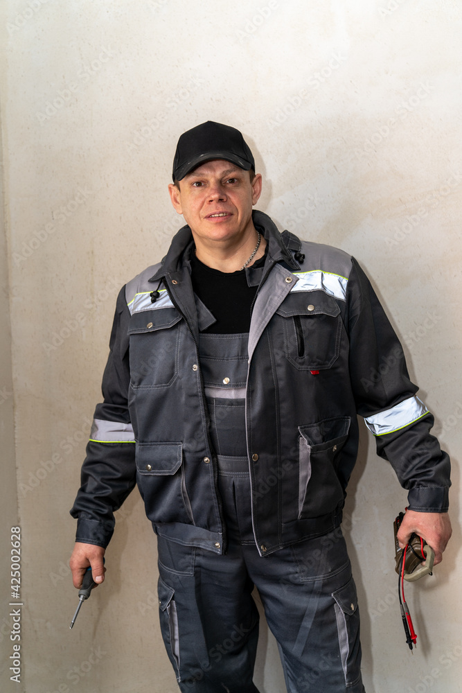 electrician in special clothing with a multimeter and a screwdriver in his hands electrician in special clothing with a multimeter and a screwdriver in his hands