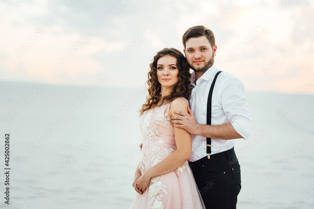 Obraz premium young couple a guy in black breeches and a girl in a pink dress are walking along the white sand