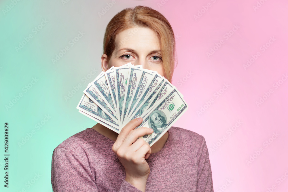 Portrait of beautiful caucasian woman holding dollars banknotes in hand and covering her face with bunch of money bills over green and red background. Portrait of beautiful caucasian woman holding dollars banknotes in hand and covering her face with bunch of money bills over green and red background.