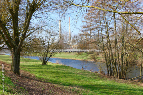 Blick auf die Enz im Enzauenpark Pforzheim, mit einer Brücke und Schornsteinen im Hintergrund photo