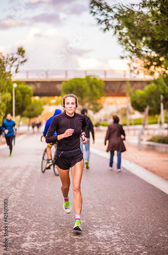 Real running woman training cardio outside for marathon listening music with headphones. Lifestyle portrait in Spain, Street outside sport.