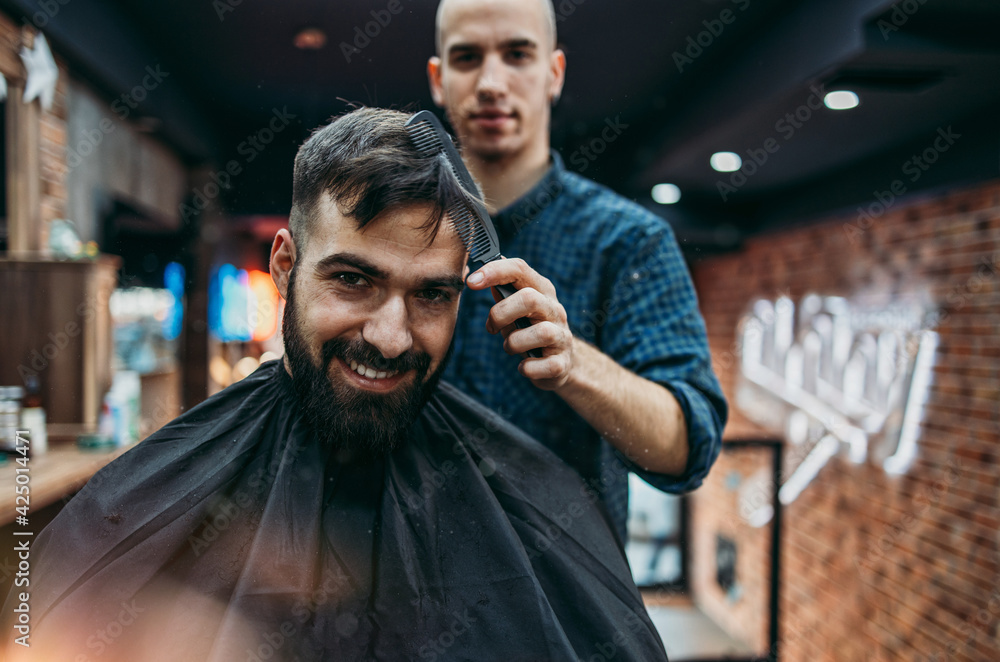 Good looking young adult man getting a hair and beard styling and dressing treatment by professional hairstylist. Good looking young adult man getting a hair and beard styling and dressing treatment by professional hairstylist.