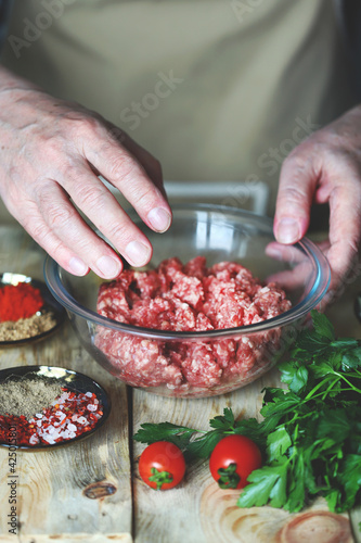 The hands of the cook stir the raw minced meat in a bowl.