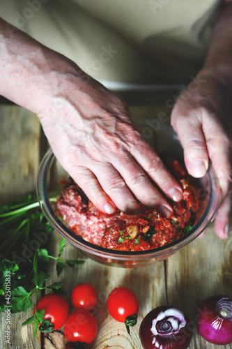 The hands of the cook stir the raw minced meat in a bowl.