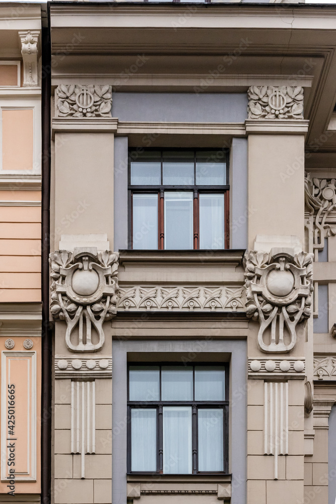 Vertical photo of detail of grey pink Art Nouveau building facade of two windows with dark frames and artsy decoration in Riga, Latvia, Europe