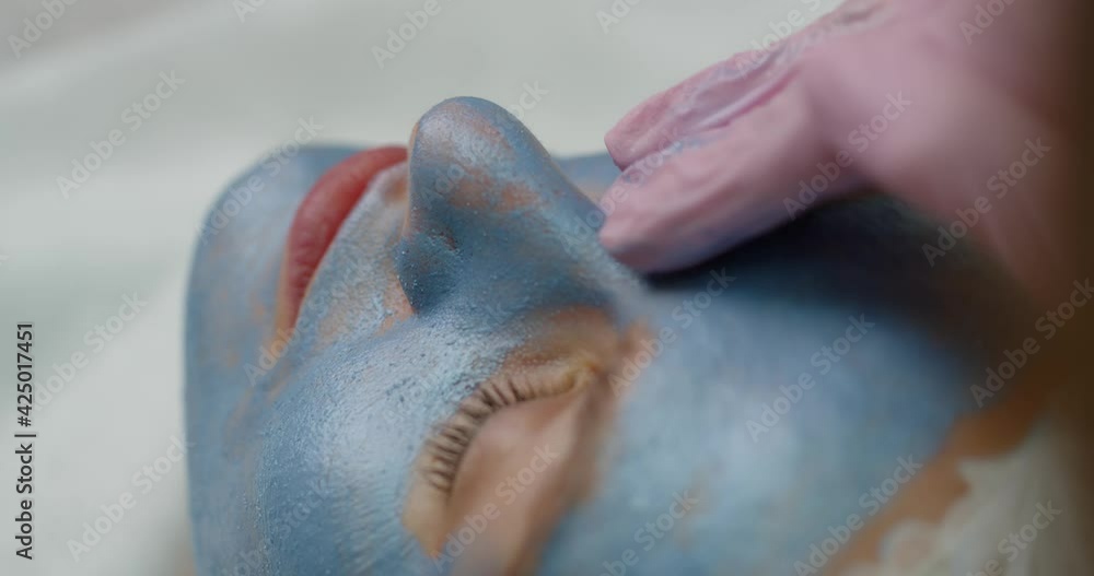 Side view of a beautician applying an innovative mask with blue clay on the skin of a beautiful young female client. The concept of salon procedures and beauty care Side view of a beautician applying an innovative mask with blue clay on the skin of a beautiful young female client. The concept of salon procedures and beauty care