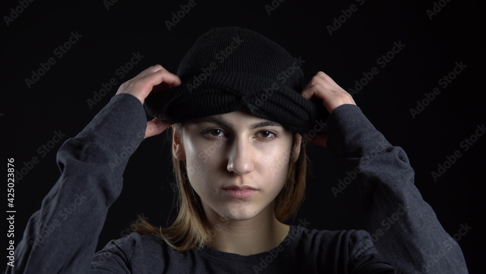 A young woman is putting on a balaclava mask. Bandit on a black background close-up. A young woman is putting on a balaclava mask. Bandit on a black background close-up.