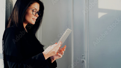 The manager is typing on the computer, a woman with glasses of European appearance. Holds the tablet. Writes down ideas for a startup project. Workplace in a coworking office for rent for an hour