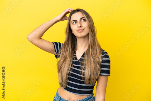 Young caucasian woman isolated on yellow background having doubts while scratching head
