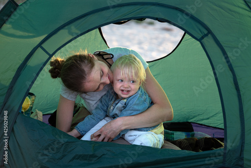 Mom hugs small child in tourist tent at the campsite. Active rest with children.