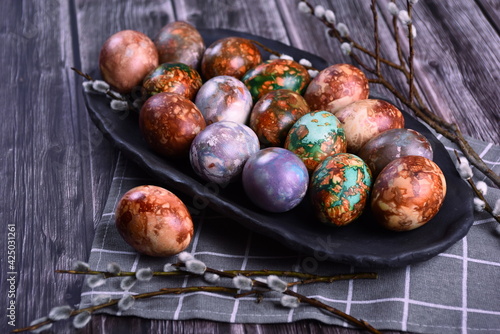 Naturally painted Easter eggs in a black clay plate on a rustic wooden background. Easter eggs painted with onion skins