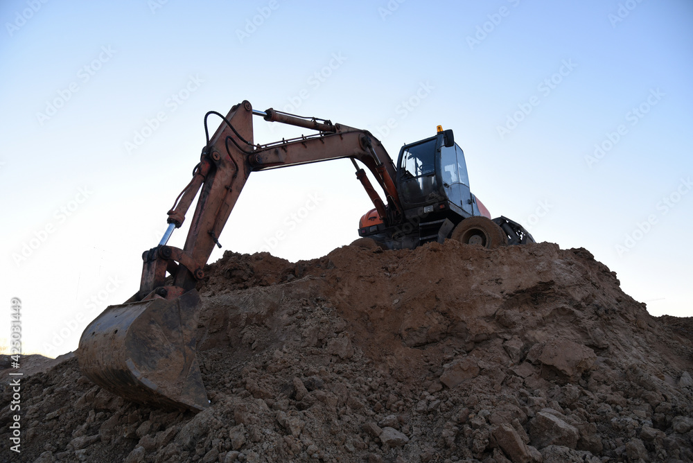 Excavator during earthmoving at open pit on blue sky background. Construction machinery and earth-moving heavy equipment for excavation, loading, lifting and hauling of cargo on construction site Excavator during earthmoving at open pit on blue sky background. Construction machinery and earth-moving heavy equipment for excavation, loading, lifting and hauling of cargo on construction site