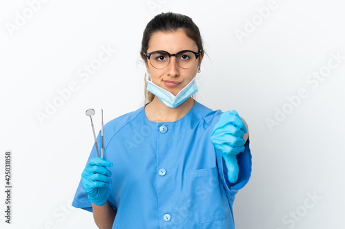 Young woman dentist holding tools isolated on white background showing thumb down with negative expression