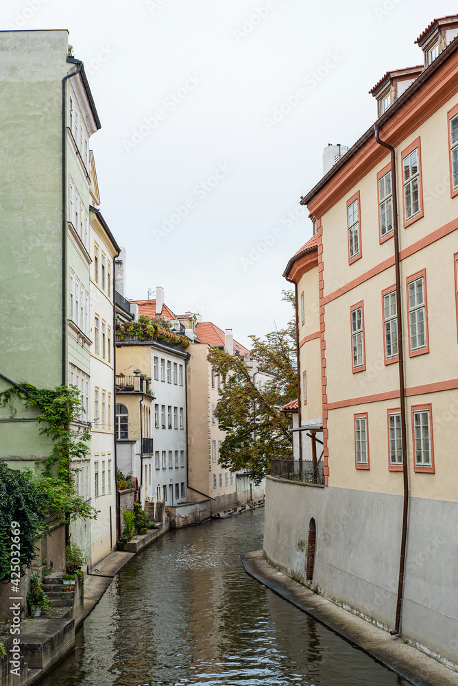 Narrow canal, river between ancient houses in the old town in Prague, Czech Republic, Europe. European houses in greenery, with verandas and terraces.