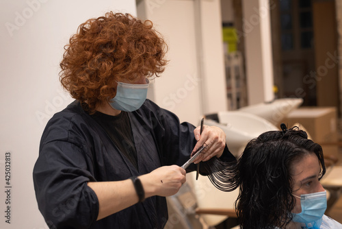 Hair cutting technique by red haired hairdresser with facemask