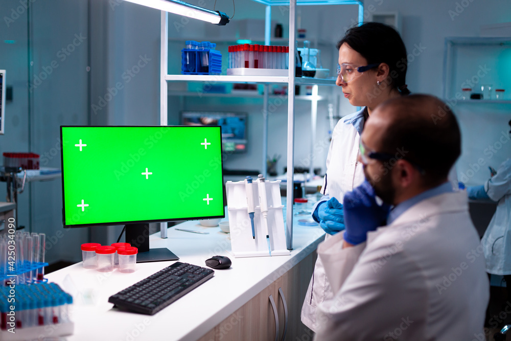 Modern medical research laboratory with two scientists using computer with green chroma key screen. Doctors specialists discovering scientifc experiment with technology equipment industry.