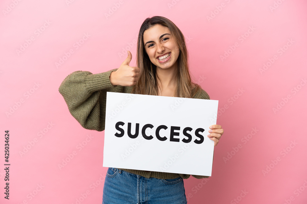 Young caucasian woman isolated on pink background holding a placard with text SUCCESS with thumb up Young caucasian woman isolated on pink background holding a placard with text SUCCESS with thumb up