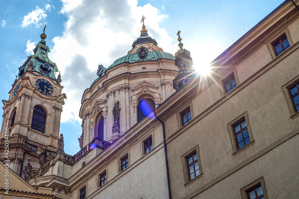 An old church, a church in Prague, Czech Republic. Clear sunny sky. The bright sun that shines into the frame. Green domes. Ancient architecture.