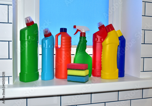 Detergent and sponge on the windowsill against the background of white ceramic tiles. Detergents bottles and kitchen sponges. Household chemicals cleaning. Anti-bacterial liquids for ​house clean