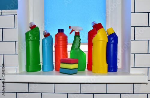 Detergent and sponge on the windowsill against the background of white ceramic tiles. Detergents bottles and kitchen sponges. Household chemicals cleaning. Anti-bacterial liquids for ​house clean