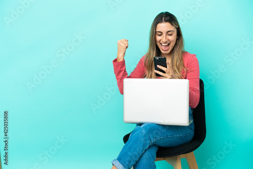 Young caucasian woman sitting on a chair with her pc isolated on blue background surprised and sending a message © luismolinero