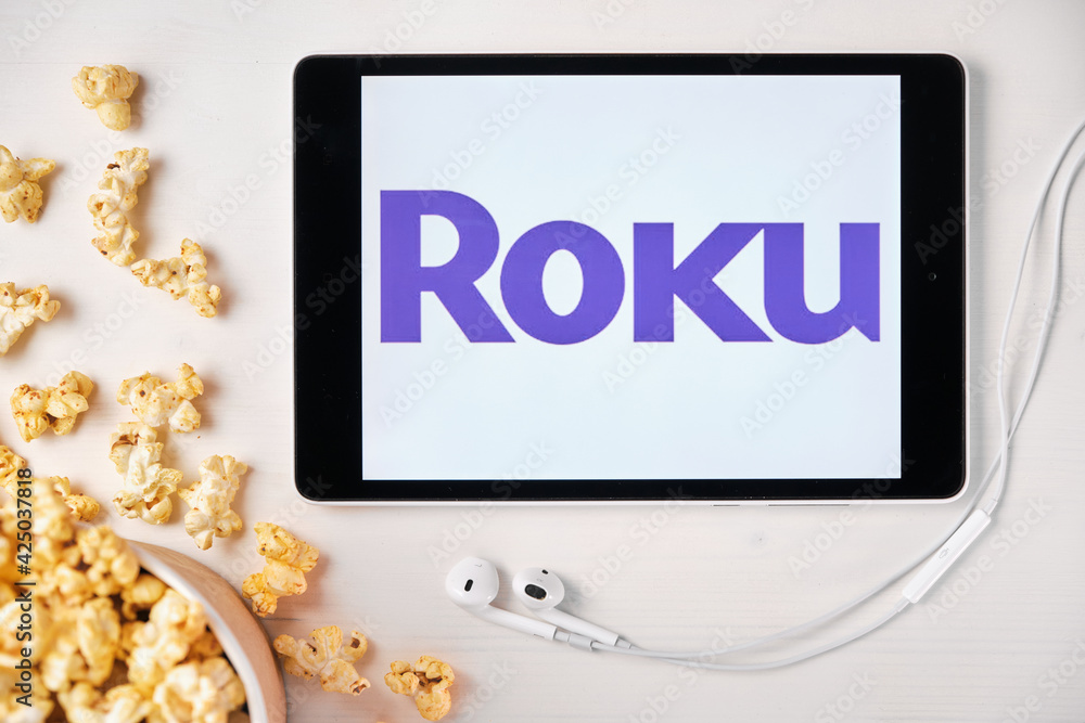 Roku logo on the tablet screen laying on the white table with scattered  popcorn and Apple earphones. Spending free time at home or news  advertisement, September 2020, San Francisco, USA. Photos