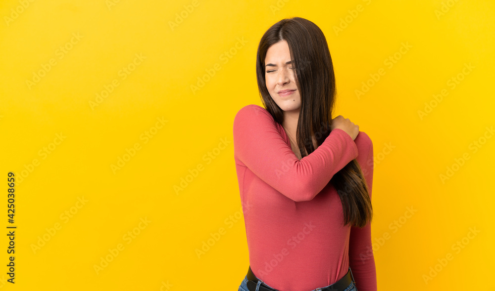 Teenager Brazilian girl over isolated yellow background suffering from pain in shoulder for having made an effort Teenager Brazilian girl over isolated yellow background suffering from pain in shoulder for having made an effort