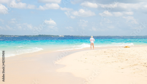 Single young woman in white shirt stands on the shore and looks out at the ocean. Back view. Natural background.