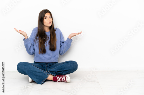 Young woman sitting on the floor having doubts while raising hands