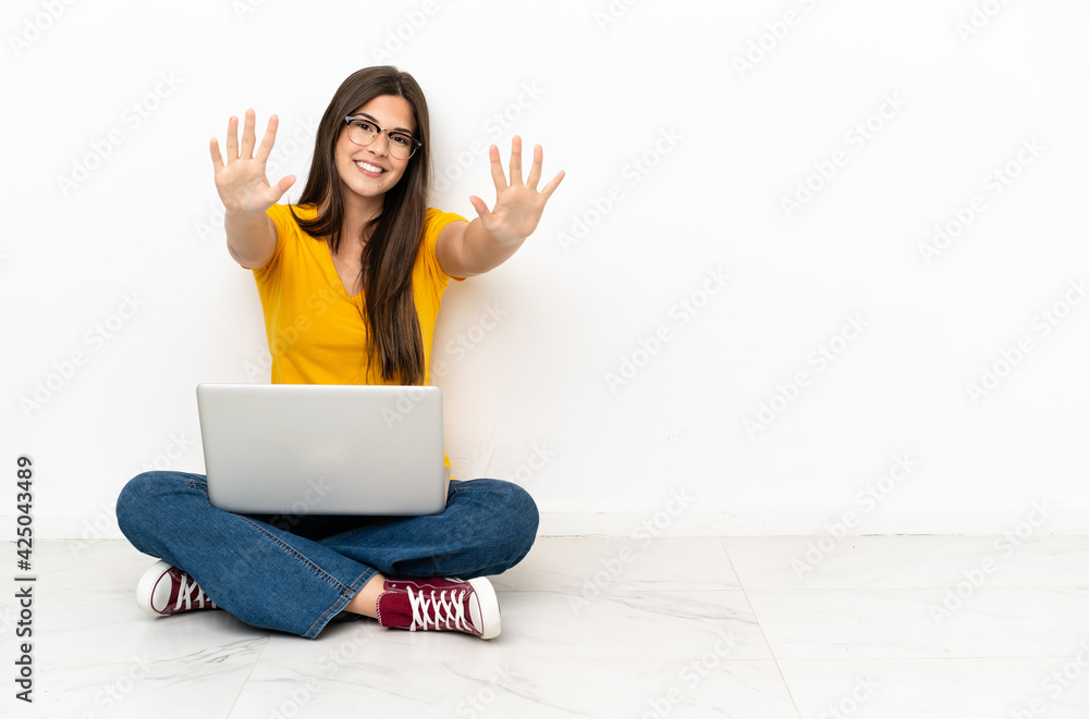 Young woman with a laptop sitting on the floor counting ten with fingers Young woman with a laptop sitting on the floor counting ten with fingers