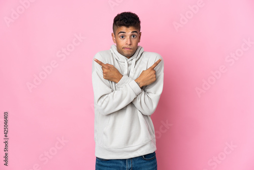 Young Brazilian man isolated on pink background pointing to the laterals having doubts © luismolinero