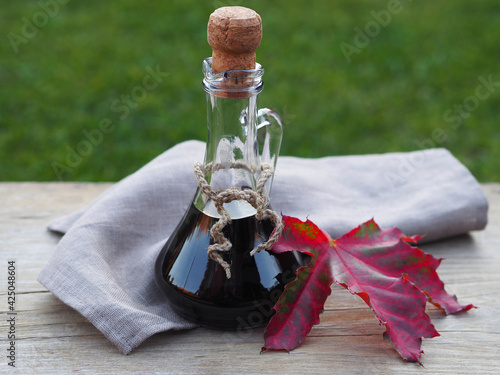 Maple syrup in a decanter and autumn red-green maple leave with a linen napkin on a wooden on the table in the garden, closeup. Bright template with natural objects and items for design photo