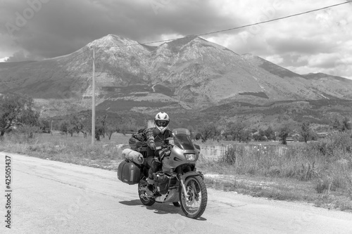 Moto Biker riding on road  drive a motorcycle  summer adventure  black and white  active lifestyle  vacation concept Magliano de Marsi  on background Riserva Naturale Orientata Monte Velino