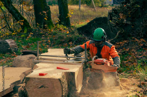 A man in an orange jacket cuts boards with an alaskan mobile chainsaw mill