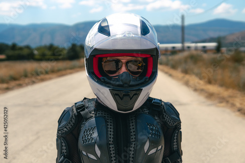 Lady Biker walking alone down the center of the road, summer adventure, active lifestyle, vacation concept. front close-up view. Sunglasses. White helmet. brutal © Sergey