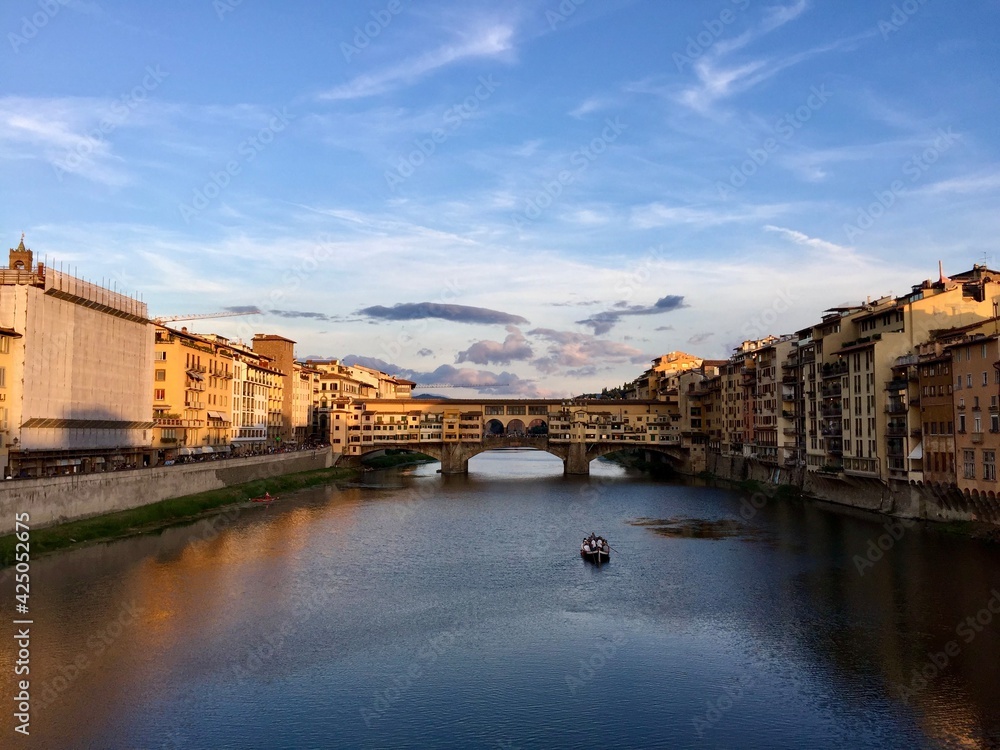 Ponte Vecchio or old bridge in Firenze and boat. Sunset with the golden bridge view in Florence. Italy. River Arno, blue sky, reflection, vessel boat. Tuscany, Toscana