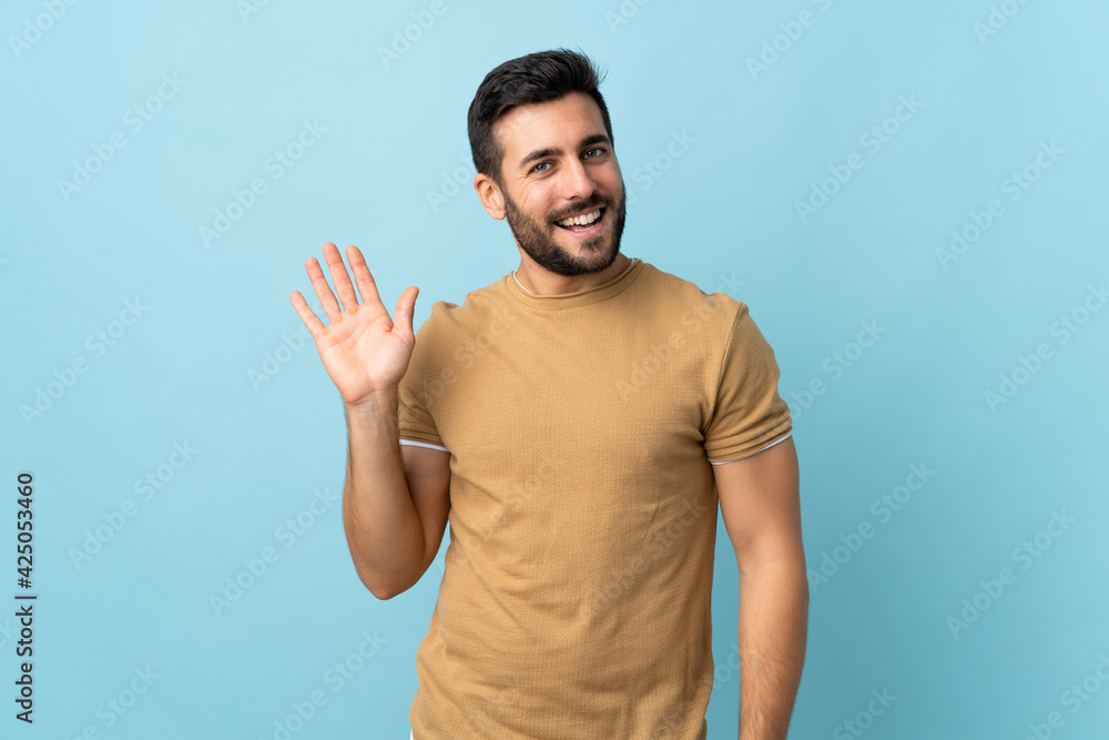 Young handsome man with beard over isolated background saluting with hand with happy expression Young handsome man with beard over isolated background saluting with hand with happy expression