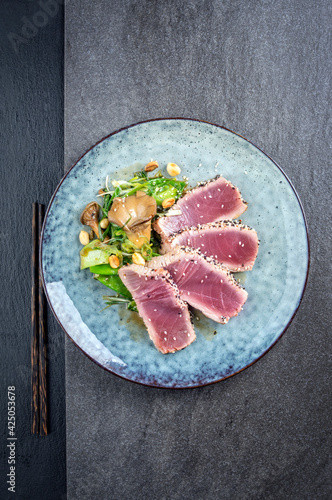 Modern style traditional Japanese tuna tataki with vegetable and mushrooms served as top view on a design plate with copy space