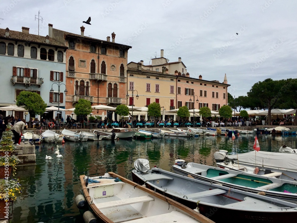 Desenzano del Garda, Italy. Marina with boats. Beautiful colorful buildings around. Reflection in water. White swan. Cloudy weather. Porto vecchio di Desenzano 