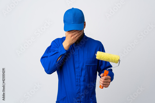 Painter man holding a paint roller isolated on white background with tired and sick expression