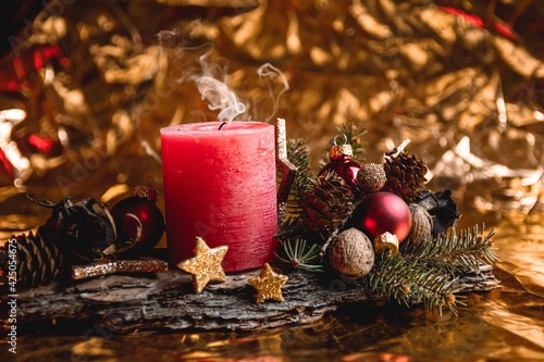 Wreath with a red candle, gold stars, ornaments on a tree bark, golden background