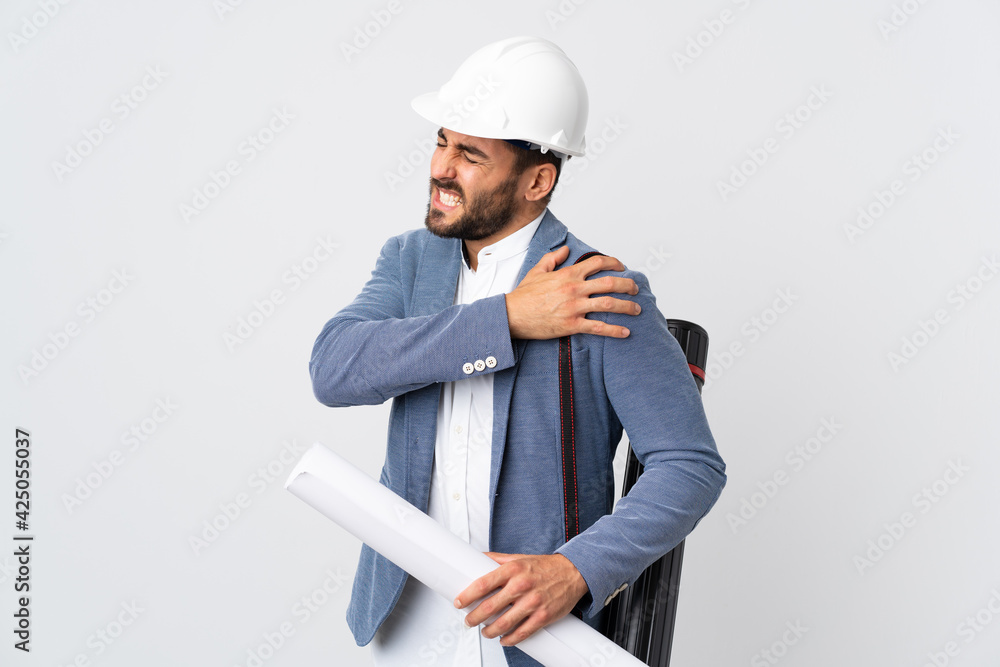 Young architect man with helmet and holding blueprints isolated on white background suffering from pain in shoulder for having made an effort Young architect man with helmet and holding blueprints isolated on white background suffering from pain in shoulder for having made an effort