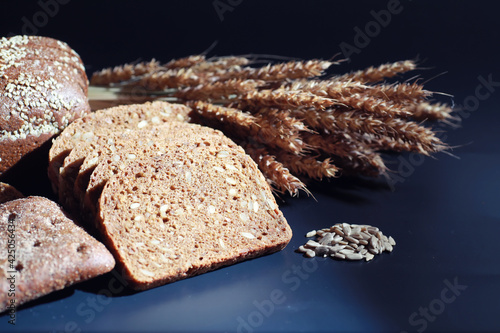 Fresh loaves of bread with wheat and gluten on a black table. Bakery and grocery concept. Fresh, healthy sorts of rye and white loaves food closeup. Fresh homemade bread with cereals.