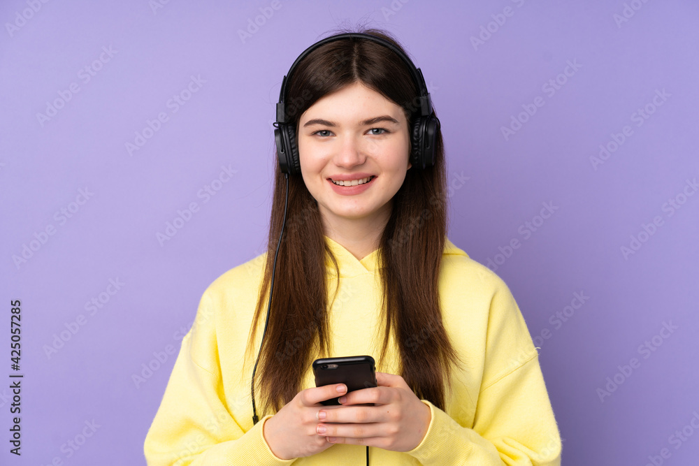 Young Ukrainian teenager girl over isolated purple background listening music with a mobile and looking front Young Ukrainian teenager girl over isolated purple background listening music with a mobile and looking front