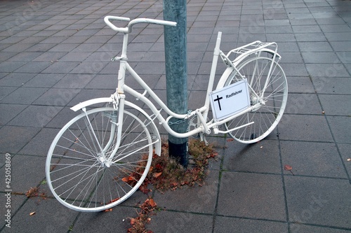 ghost bike memorial with a cross sign for a killed cyclist at Frankfurt Main, Germany streets on a rainy Dreary Day. White ghost bicycle, memorial to a cyclist who died in traffic accident