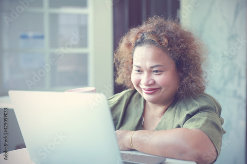 Asian Businesswomen adult sitting smiled happily have high self-confidence holding pink mug coffee looking at the laptop on a table at the house.