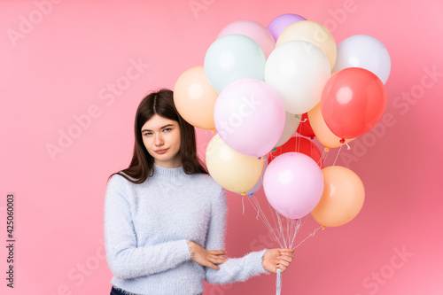 Young Ukrainian teenager girl holding lots of balloons over isolated pink background thinking an idea